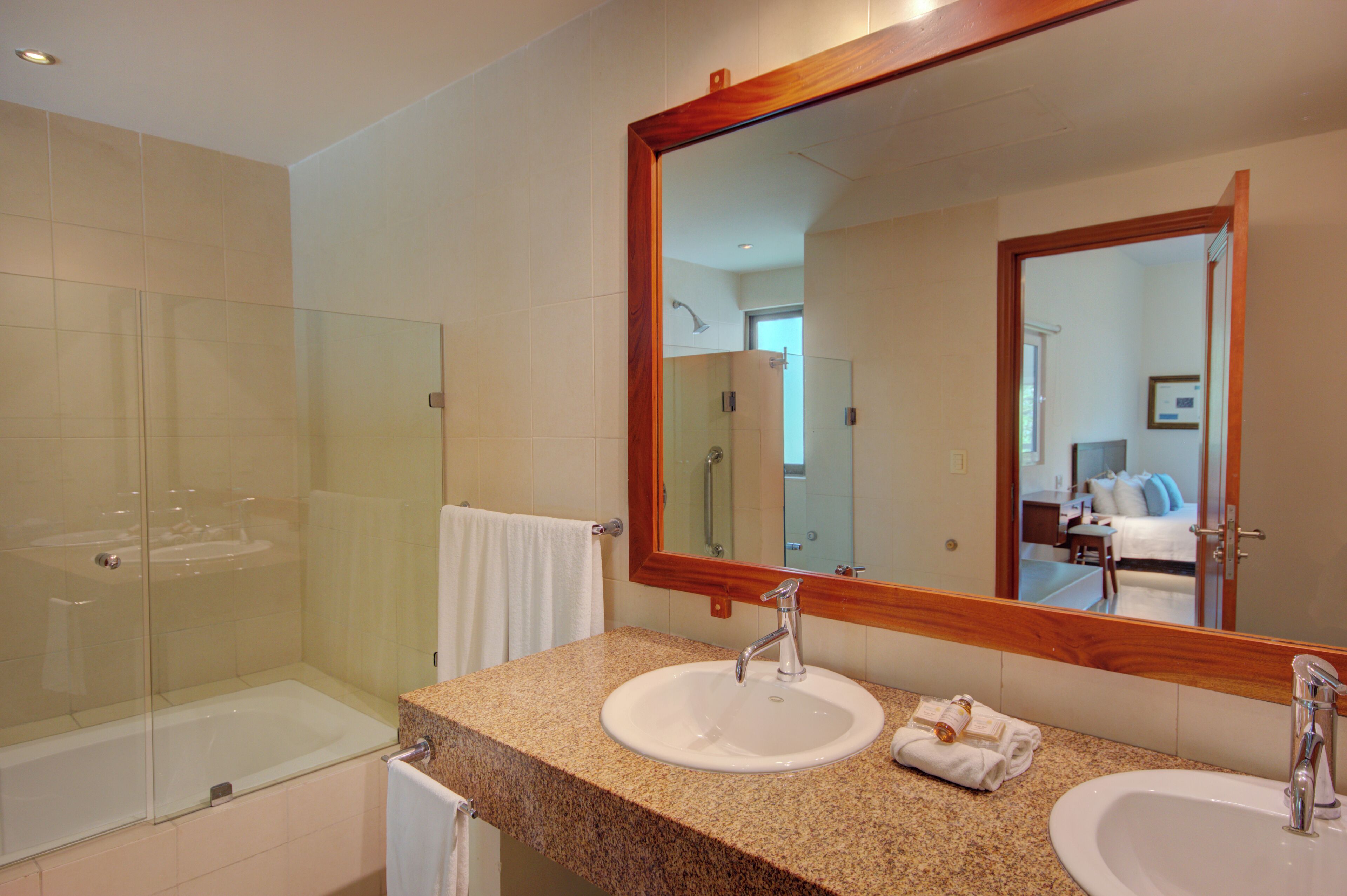 A bathroom with a glass-enclosed shower, two sinks, and a large mirror.