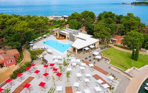 Eine Vogelperspektive eines Resorts mit Schwimmbad, Sitzbereichen im Freien und Blick aufs Meer.
