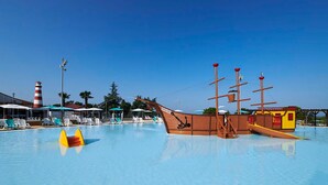Une piscine dotée d’un espace de jeux sur le thème des bateaux, de chaises longues et d’un phare en arrière-plan.