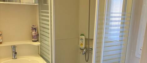 Un baño con lavamanos blanco, cabina de ducha de vidrio y alfombrilla de baño azul.