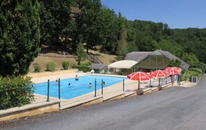 A swimming pool with a fenced area, surrounded by greenery and a building with red umbrellas.