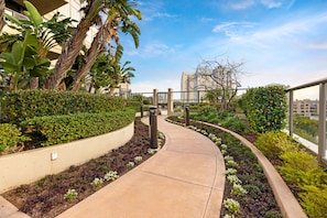 A curved pathway flanked by landscaped gardens with various plants and a building in the background. - Electra Building 2bed - Views, Pool, Sauna, Spa (San Diego)