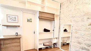 Ein Zimmer mit Holzboden, einem weißen Schreibtisch, einem Kleiderschrank mit Kleiderstange und einem Spiegel an der Wand.