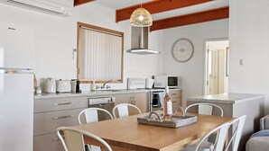 A modern kitchen with white cabinetry, a wooden dining table, and a hanging light fixture.