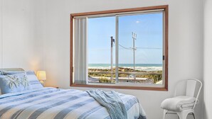 A bedroom with a large window overlooking a beach, a bed with striped bedding, and a chair.