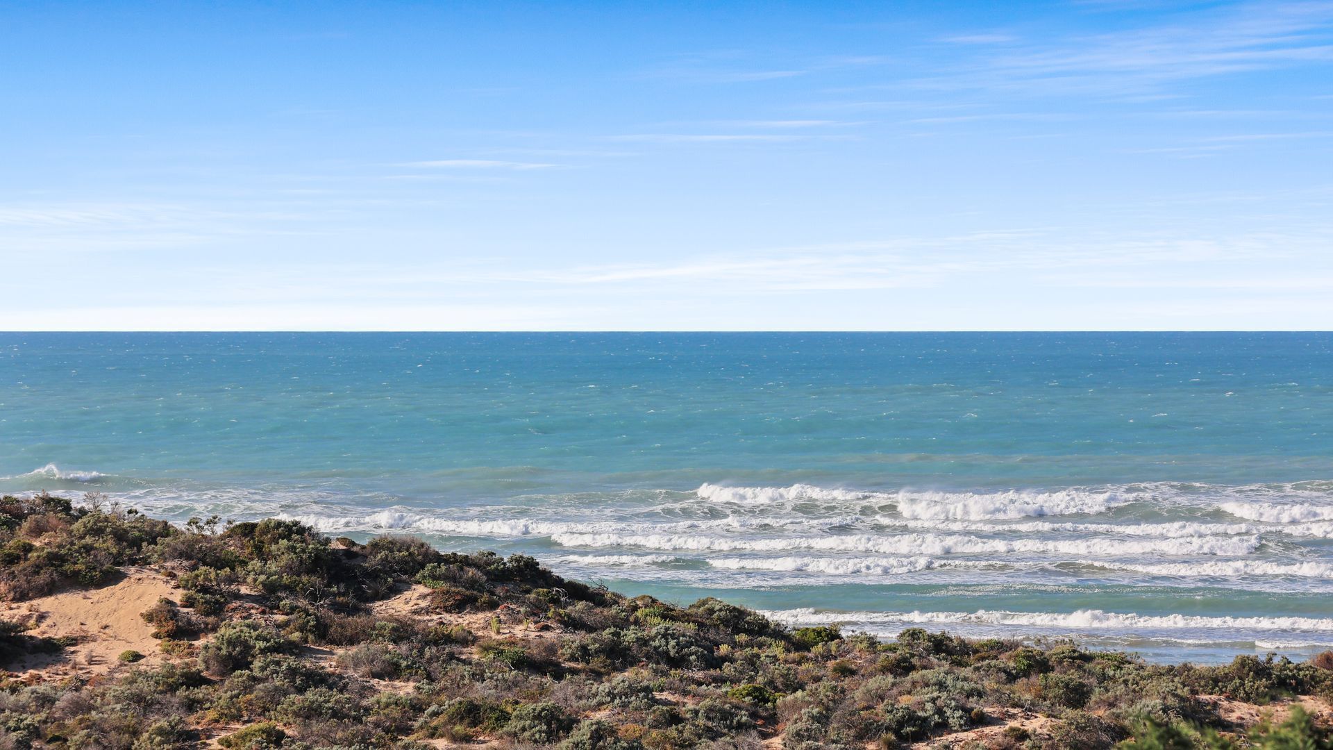 Et kystlandskab med udsigt over havet og en sandstrand med sparsom vegetation.