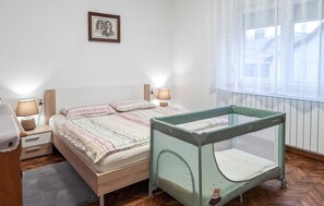 A bedroom with a bed, bedside lamps, a crib, a window with sheer curtains, and a framed picture on the wall. - Nice apartment in Delnice with WiFi (Delnice)