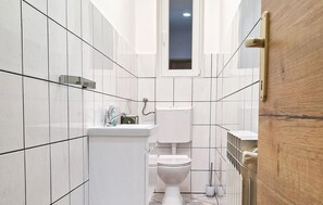 A narrow bathroom with white tiles, a toilet, a sink, and a window above the toilet. - Nice apartment in Delnice with WiFi (Delnice)
