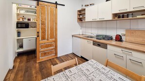 A compact kitchen with white cabinets, a wooden door, a microwave, a dishwasher, and a table with a printed tablecloth. - Nice apartment in Delnice with WiFi (Delnice)