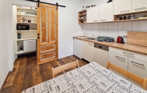 A compact kitchen with white cabinets, a wooden door, a microwave, a dishwasher, and a table with a printed tablecloth. - Nice apartment in Delnice with WiFi (Delnice)