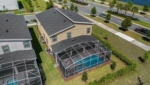 Un quartier résidentiel où se trouve une maison dotée d’une grande piscine couverte, entourée de pelouses et d’arbres bien entretenus.