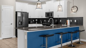 Une cuisine moderne avec des meubles blancs, un plan de travail noir et un îlot central bleu doté de tabourets de bar.