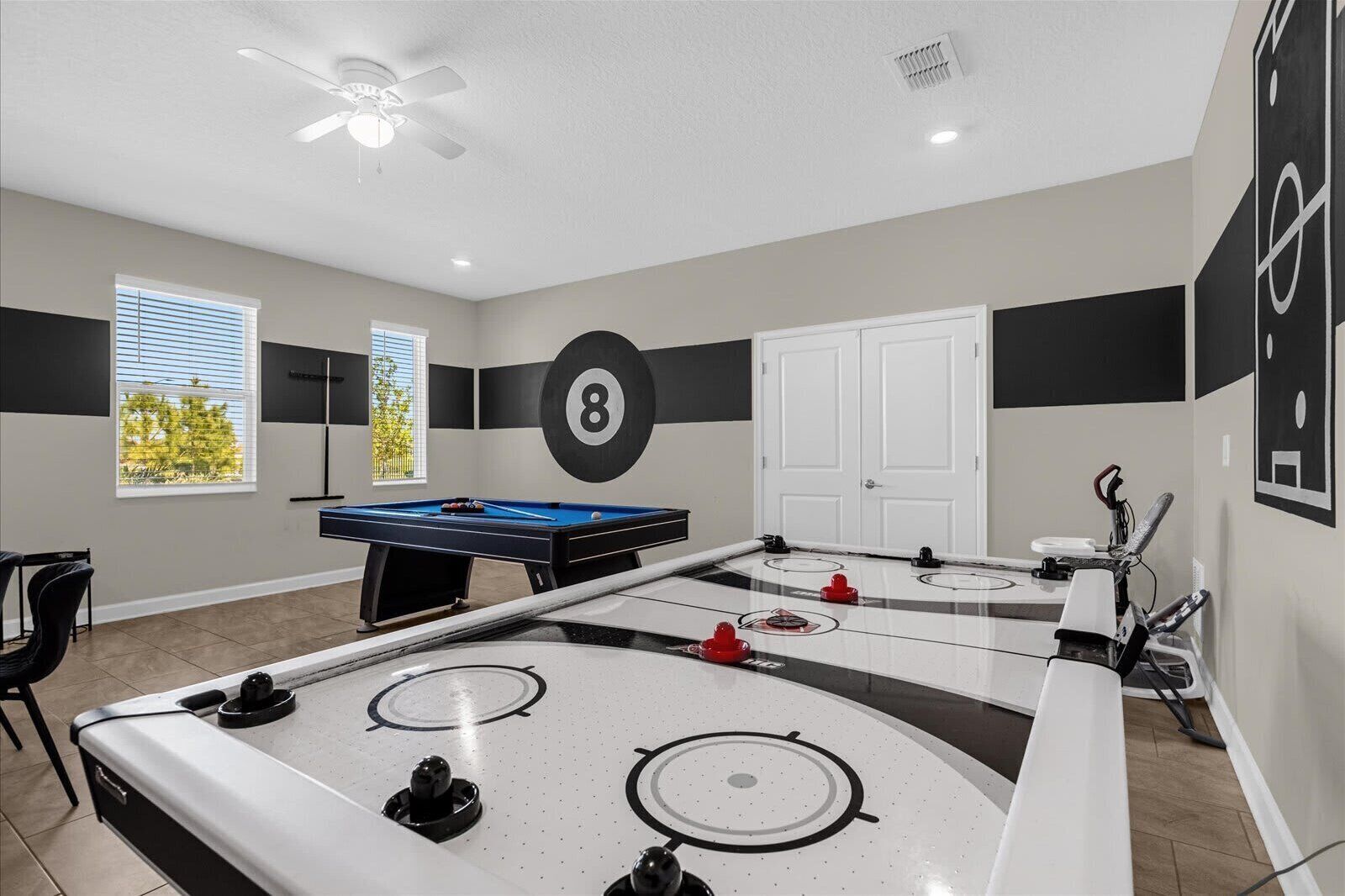 A room with a pool table, foosball table, and a ceiling fan.