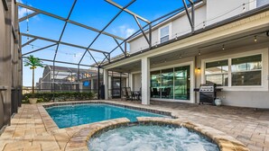Ein Schwimmbecken mit Whirlpool, umgeben von einer Terrasse mit Gartenmöbeln und einem überdachten Bereich mit Grill.