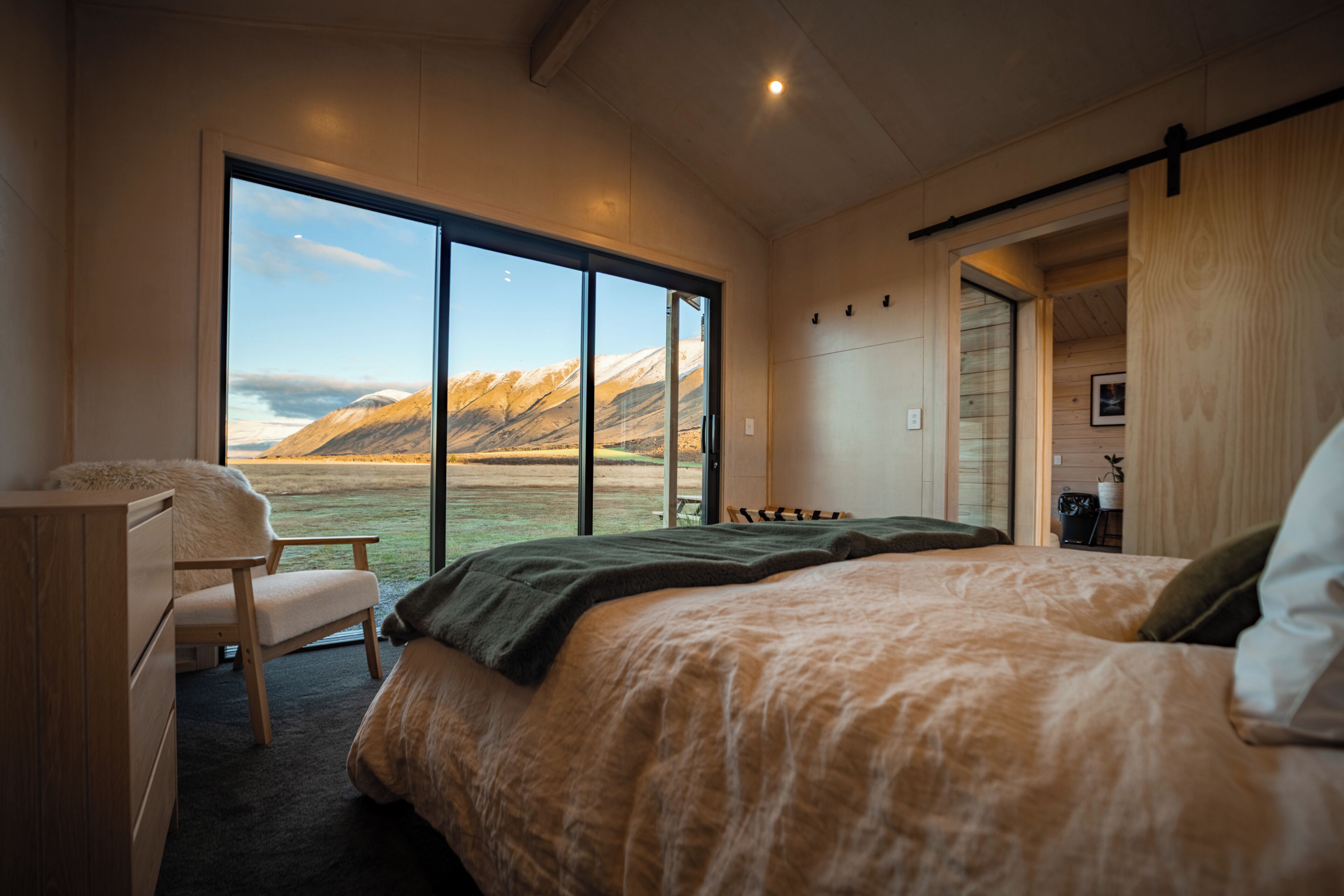 A bedroom with a large window, a bed, a chair, and a desk.