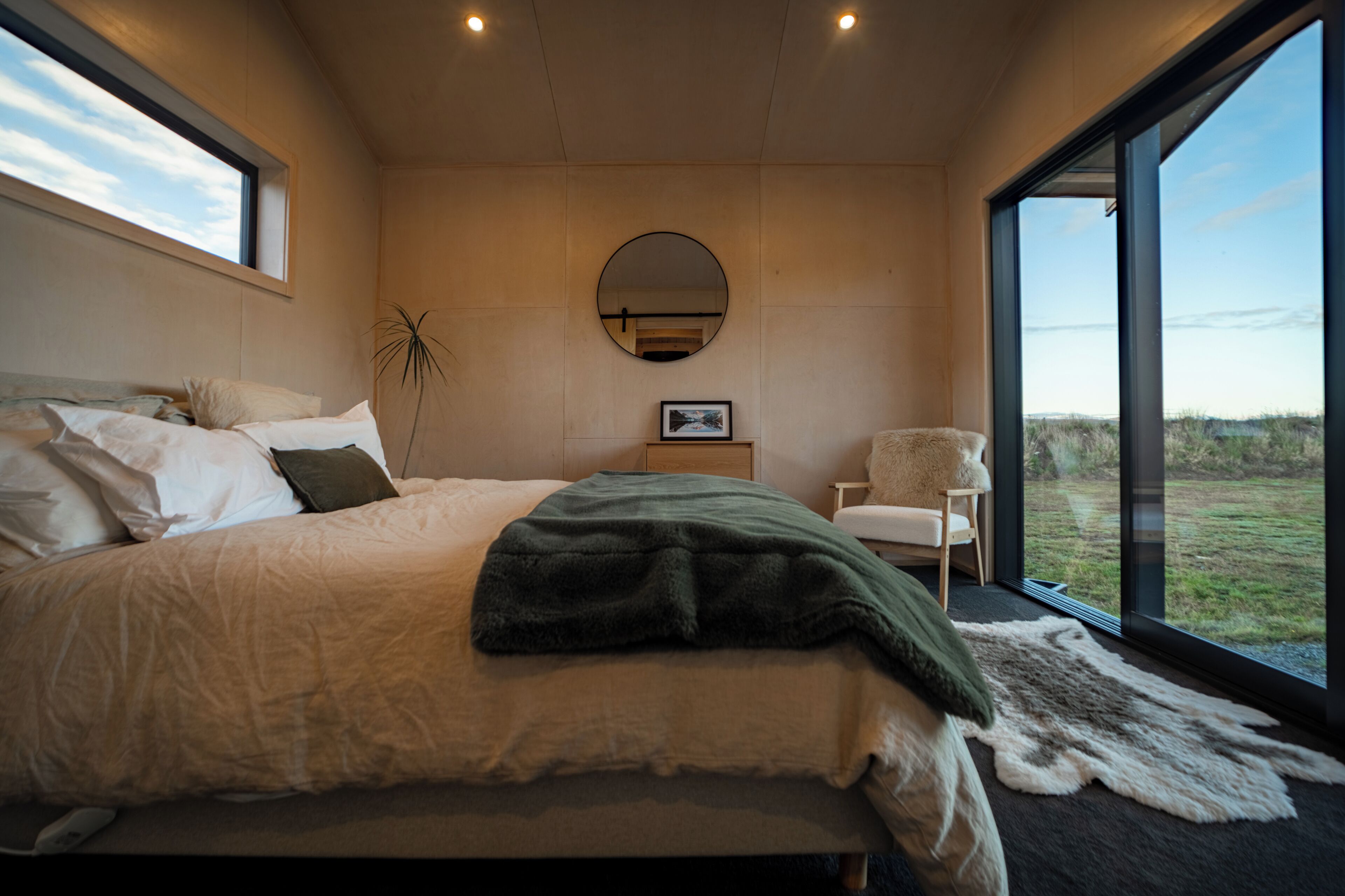 Quarto com uma cama grande, uma cadeira, um espelho e vista para o exterior.