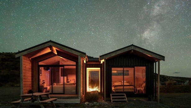 Two wooden cabins with open fronts, a fire feature, and a starry night sky.