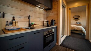 A compact kitchen with a sink, stove, and countertop, leading to a bedroom with a bed and a round mirror.