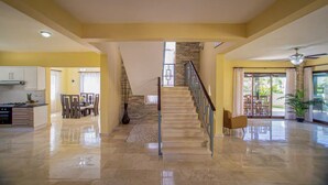 A spacious living area with a polished stone floor, a staircase with a glass railing, and a dining area with chairs and a table. - 6 bedroom Villa steps from the beach (Sosúa)