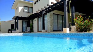 A modern two-story house with a swimming pool, a covered patio, and a garden with red flowers. - 6 bedroom Villa steps from the beach (Sosúa)