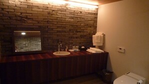 Un baño con tocador de madera, lavamanos, espejo, toallero y retrete.