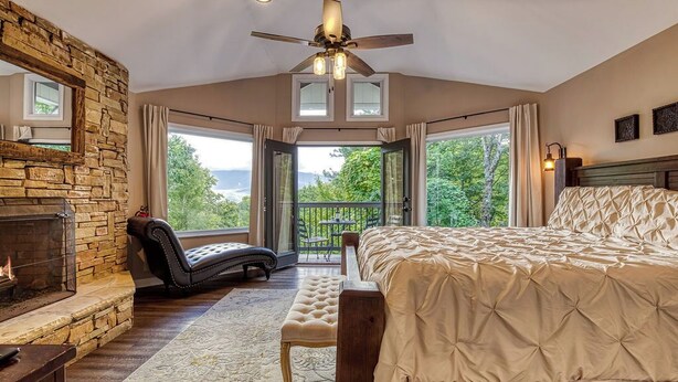 A bedroom with a stone fireplace, a bed, a bench, and a view of the outdoors. - 2BR/2BA, 2 Fireplaces, Hot Tub, 10 Minutes from Downtown and GSMNP, No Pet Fee! (Gatlinburg)