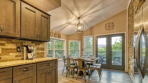 A spacious kitchen with dark wooden cabinets, a granite countertop, and a built-in coffee maker. There is a dining area with a table and chairs, and large windows offering a view of the outdoors. - 2BR/2BA, 2 Fireplaces, Hot Tub, 10 Minutes from Downtown and GSMNP, No Pet Fee! (Gatlinburg)