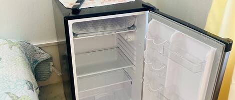 Un refrigerador compacto con compartimento congelador, panel de control y una pequeña encimera con dos vasos y un control remoto.