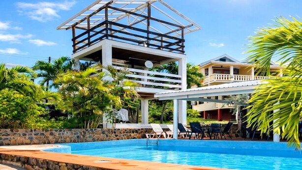 A swimming pool with lounge chairs, a stone wall, and a building with a balcony.