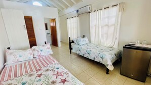 A room with two beds, a small kitchenette, and a ceiling fan.