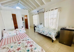 Un dormitorio con dos camas, un refrigerador pequeño y un baño a la vista.