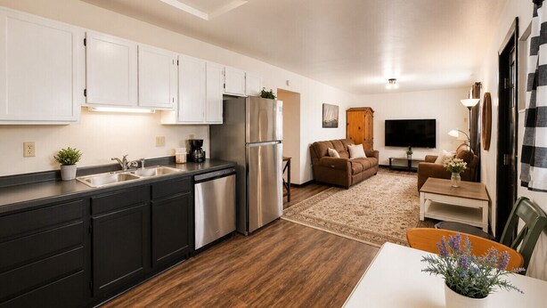 A modern kitchen with dark cabinetry, stainless steel appliances, and a wooden floor. - Sun-Filled Home | Walk to Downtown & Dining (Rapid City)