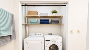 A laundry room with two white washing machines, a shelf with folded towels, and a potted plant. - Sun-Filled Home | Walk to Downtown & Dining (Rapid City)