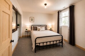 Un dormitorio con cama, mesitas de noche, un espejo, una ventana con cortinas y una lámpara en el techo.