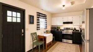 A compact kitchen with a dining area, a black door, white cabinets, a microwave, an oven, and a refrigerator. - Sun-Filled Home | Walk to Downtown & Dining (Rapid City)