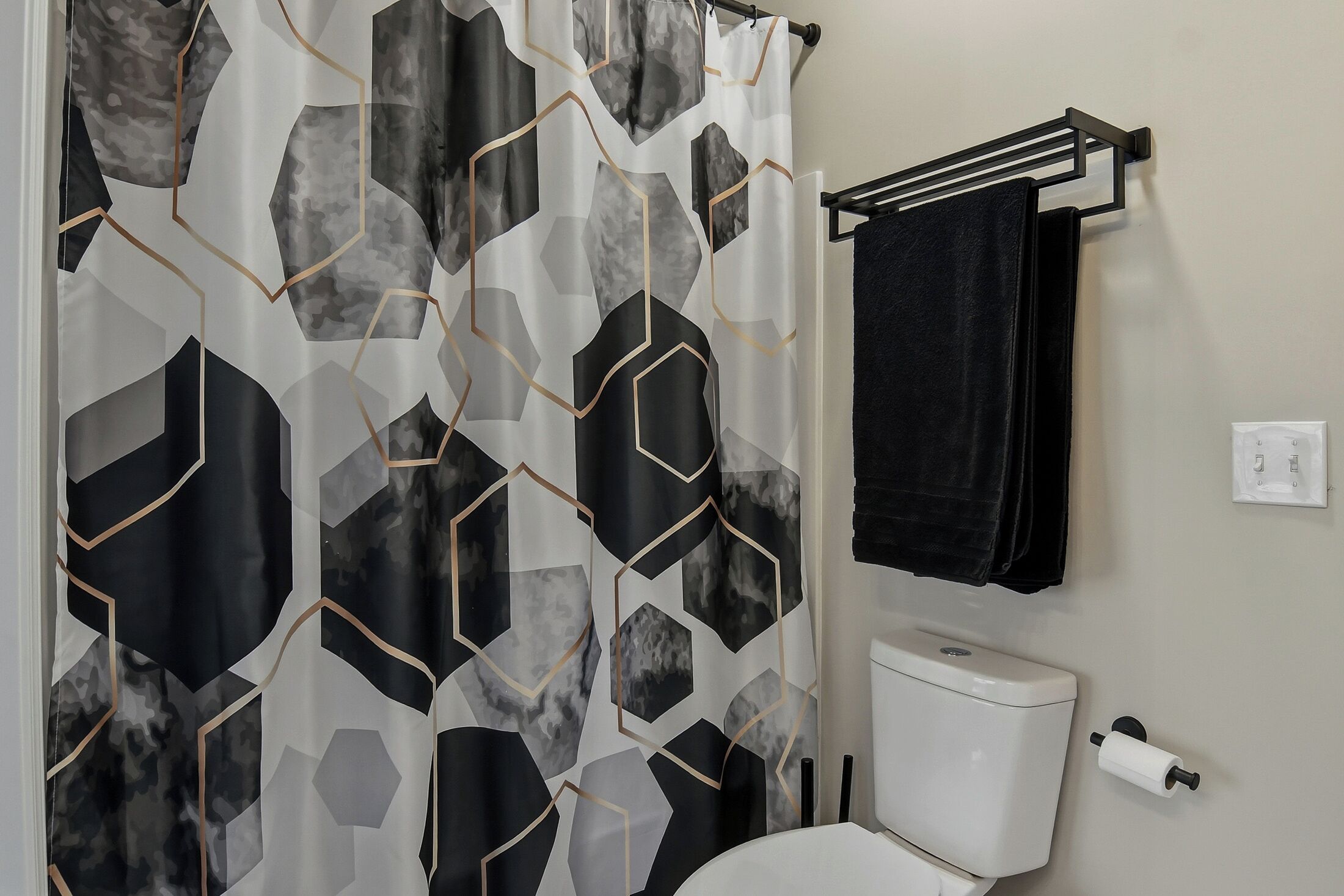A bathroom with a geometric shower curtain, a toilet, and a towel rack with a black towel.