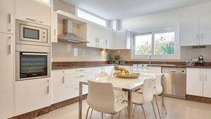 A modern kitchen with white cabinets, stainless steel appliances, and a dining area with a table and chairs. - Villa Julieta – Ibiza Town (2 min) (Nuestra Señora De Jesus)