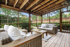 En overdækket terrasse med udendørs møbler i flet, en hvid sofa og et træbord.
