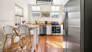 A kitchen with a stainless steel refrigerator, a dishwasher, a stove, and a dining area with wicker chairs. - Colorful House w. Outdoor Space + Parking (Charleston)