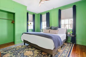 Une chambre avec un grand lit, des murs verts, un plancher en bois et un tapis à motifs.