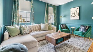 A living room with teal walls, a beige sectional sofa, a wooden coffee table, and green armchairs. - Colorful House w. Outdoor Space + Parking (Charleston)