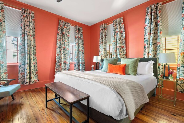 Une chambre avec un grand lit, des rideaux à motifs floraux, un plancher en bois et un banc.
