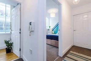 A hallway with a wooden floor, a potted plant, a white door, and a staircase with a blue railing. - Manchester City Center | Free Parking + Wi‑Fi (Manchester)