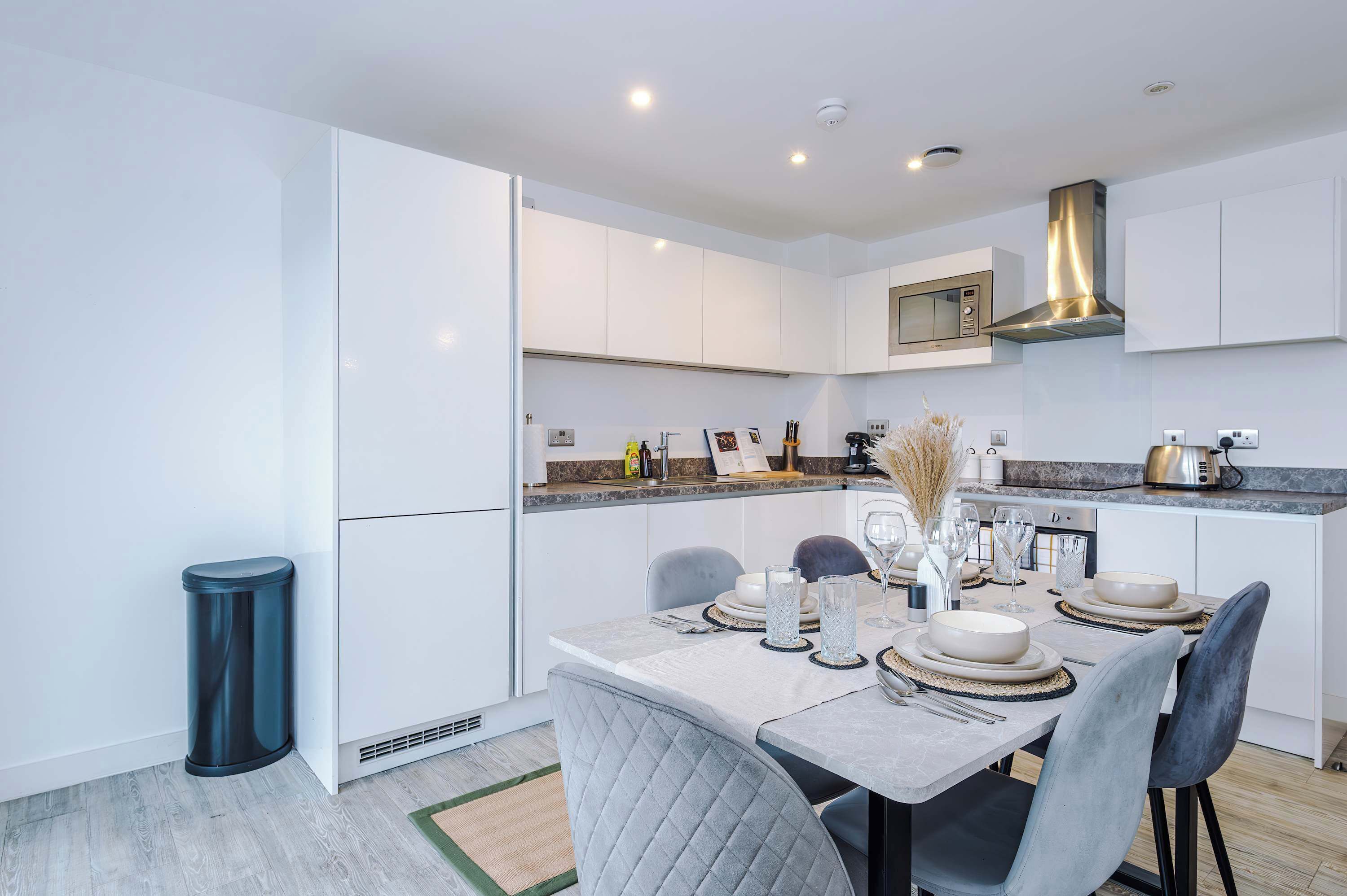 A modern kitchen with white cabinets, a stainless steel range hood, and a dining area with a table set for four.