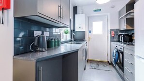 A modern kitchen with grey cabinets, a stainless steel range hood, a kettle, and a microwave.
