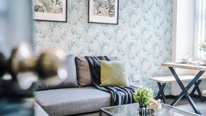 A modern living room with a grey sofa, a glass coffee table, and a dining area with a wooden table and chairs.