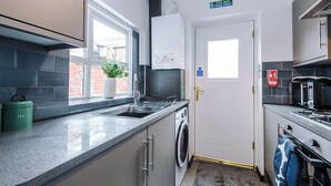 A compact kitchen with a built-in washing machine, a coffee maker, and a window providing natural light.