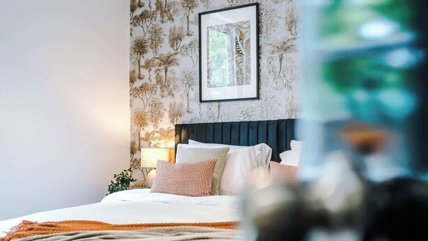 A neatly made bed with a white and orange blanket, a dark headboard, and a framed picture on the wall.
