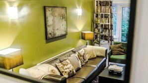 A modern living room with a green wall, a leather sofa, a bookshelf, and a window with curtains. - 5BR Contractor House | Free Parking | Near Airport (Manchester)