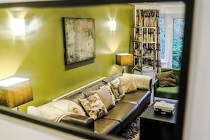 Una sala de estar moderna con una pared verde, un sofá de cuero, una estantería y una ventana con cortinas.